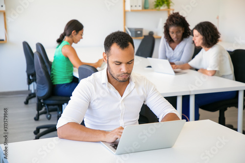 Serious young man typing on laptop. Focused young managers working at office. Technology concept