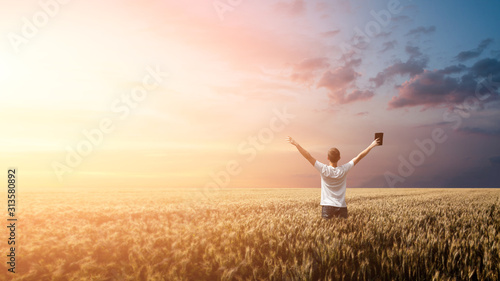 Man holding up Bible in a wheat field during sunrise. panoramic shot