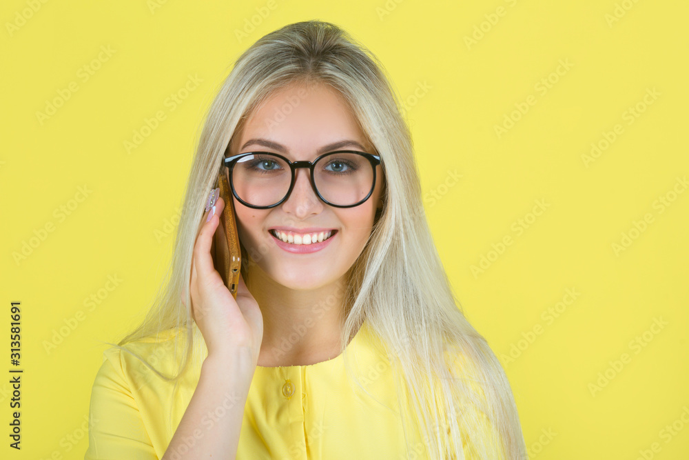 beautiful young woman in a yellow dress on a yellow background in glasses with a phone in her hand