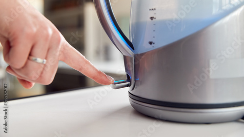 Close Up Of Woman Pressing Power Switch On Electric Kettle To Save Energy At Home photo
