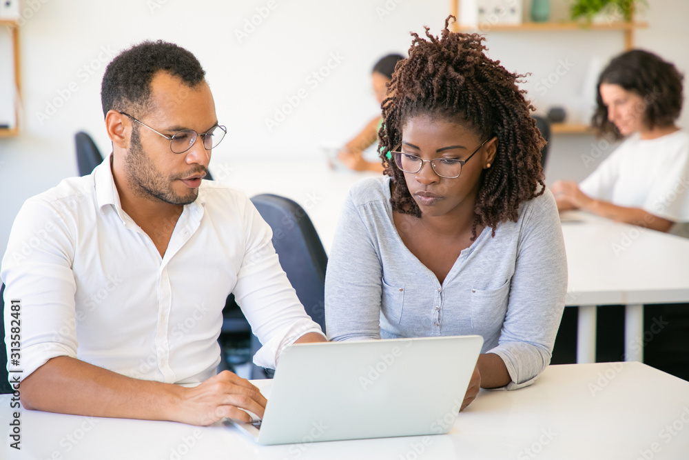 Thoughtful colleagues talking and looking at laptop. Front view of two young people working with laptop at office. Teamwork concept Thoughtful colleagues talking and looking at laptop. Front view of two young people working with laptop at office. Teamwork concept