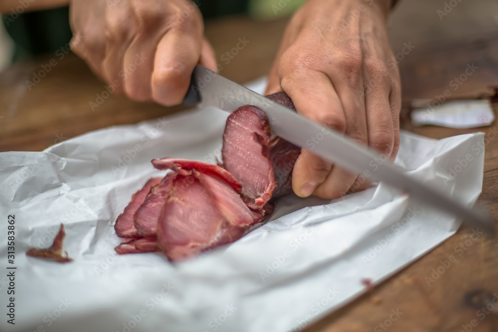 Detailed view of a hand slicing homemade pork chorizo on wooden table