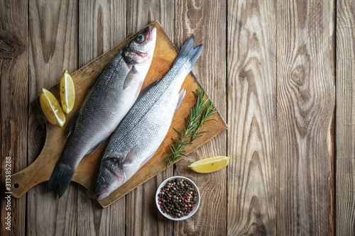 Fresh seabass and ingredients for cooking. Raw fish seabass with lemon, spices and herbs on wooden rustic table. Top view with copy space.