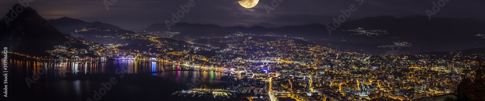Panoramica della città di Lugano di notte illuminata da una luna brillante