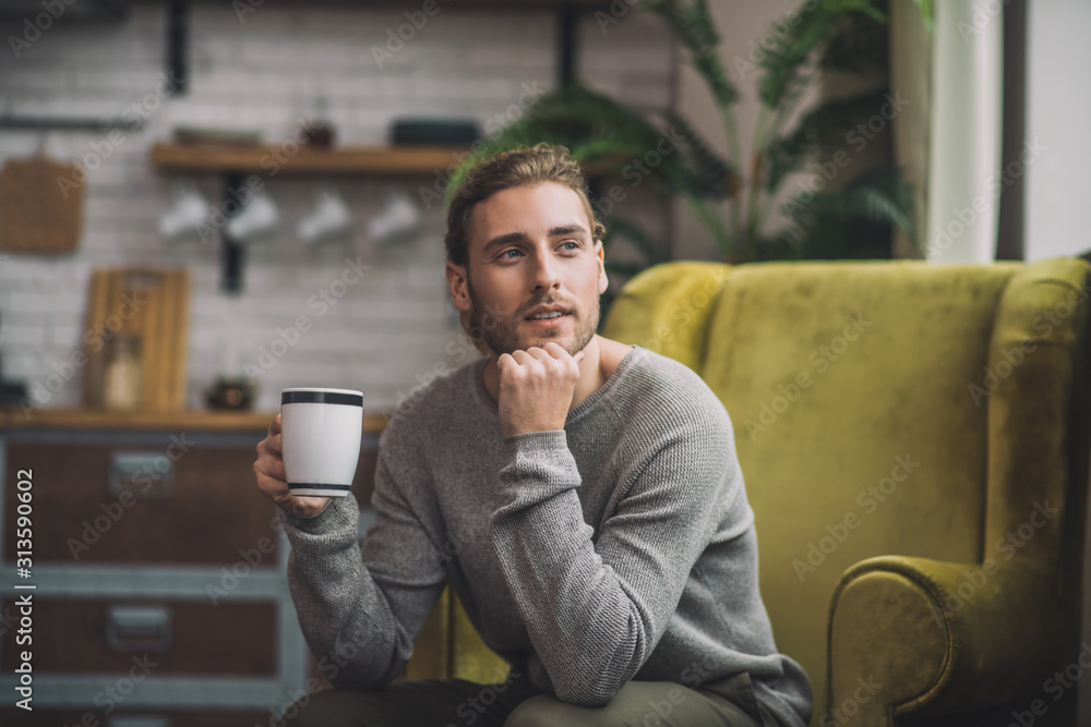 Young bearded handsome man with cup sitting in armchair Young bearded handsome man with cup sitting in armchair