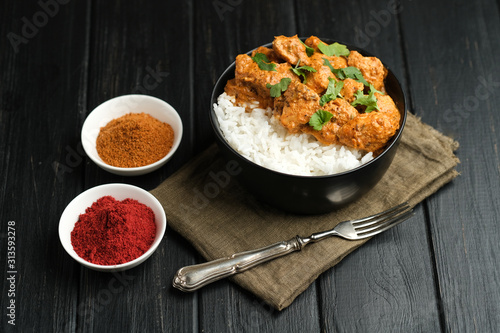 Chicken tikka masala traditional Asian spicy meat food with rice tomatoes and cilantro in a black bowl on dark wooden background.