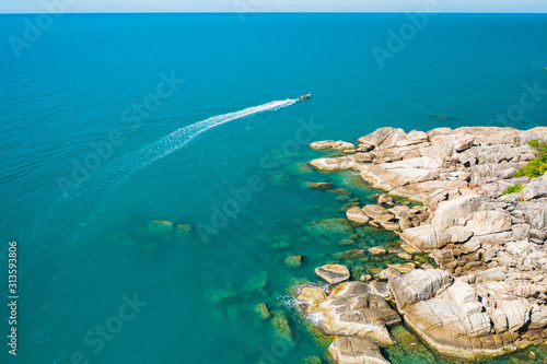 aerial drone shot of a motorized boat in turquoise coloured water along a rocky coastline, Koh Phanghan, Thailand 