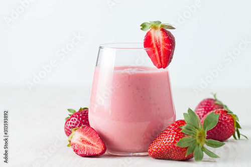 Glass of fresh strawberry milkshake, smoothie and fresh strawberries on pink, white and wooden background. Healthy food and drink concept.