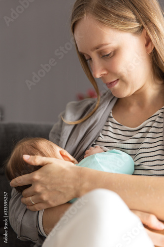 Focused Caucasian new mom breastfeeding baby. Portrait of young woman and cute little child in home interior. Maternity concept