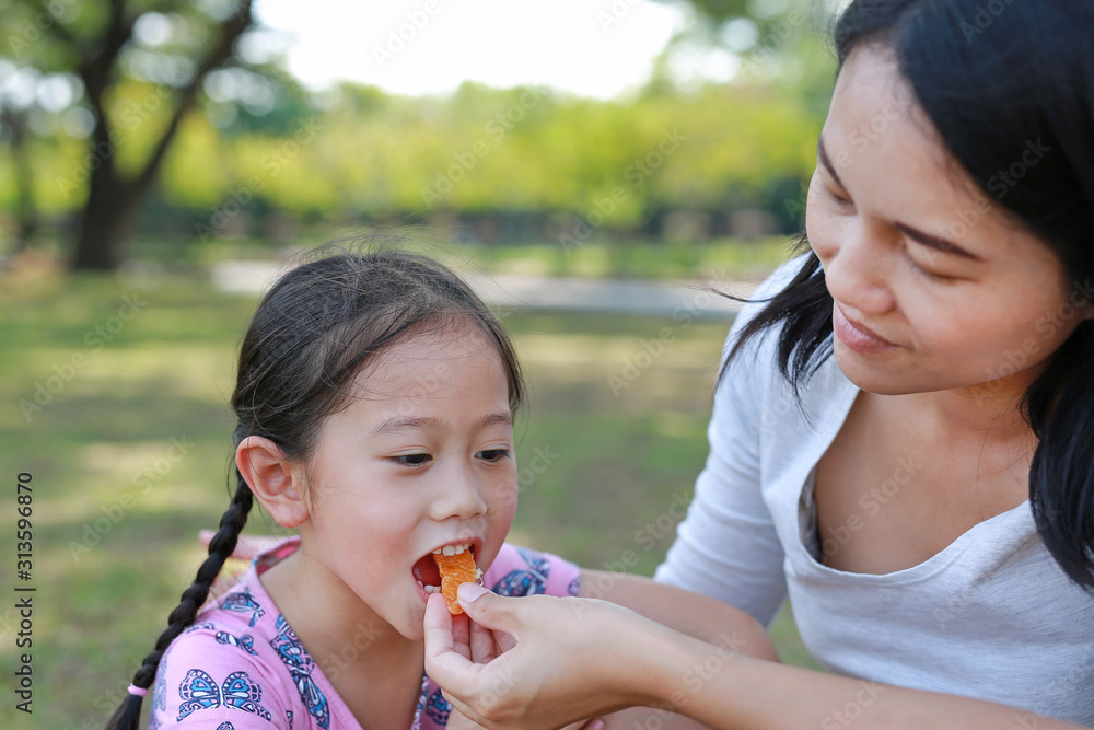 Closeup Asian mother feeds some orange fruit for her daughter in the garden outdoor. Closeup Asian mother feeds some orange fruit for her daughter in the garden outdoor.