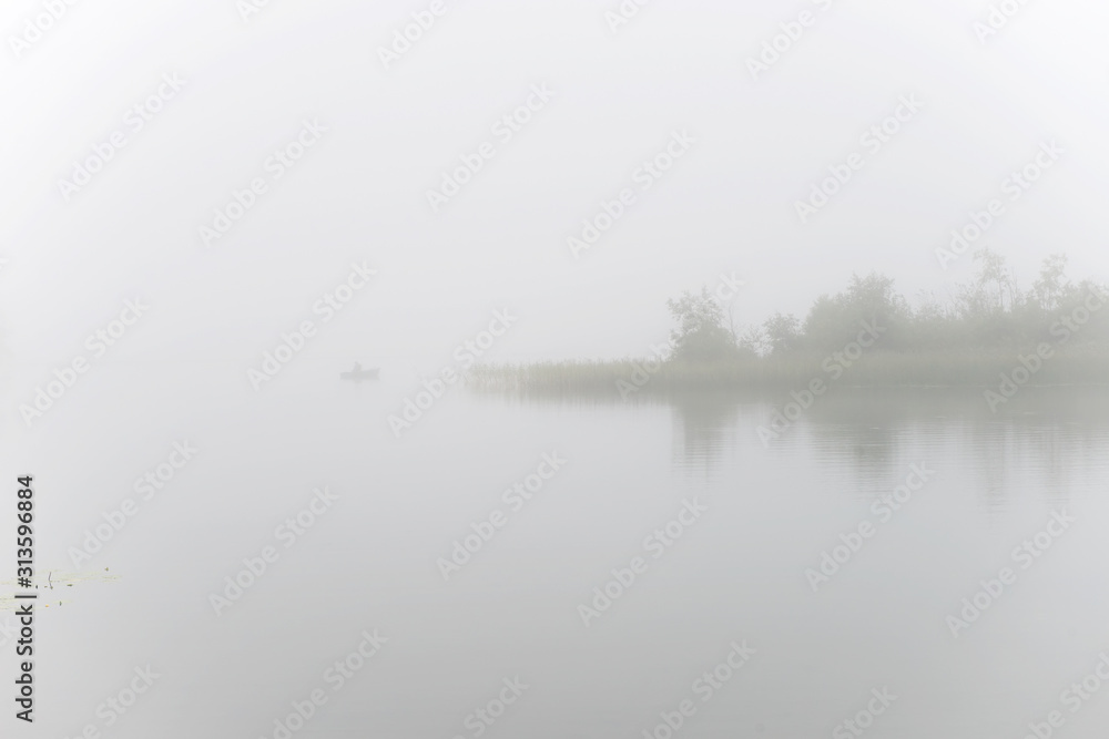 Fisherman on a boat fishing on a lake on a foggy morning Fisherman on a boat fishing on a lake on a foggy morning
