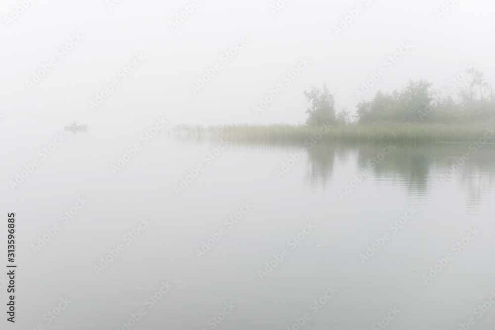Fisherman on a boat fishing on a lake on a foggy morning