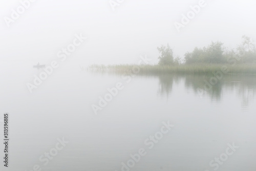 Fisherman on a boat fishing on a lake on a foggy morning