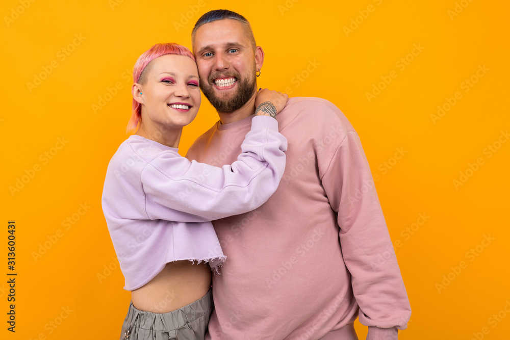 Obraz premium happy smiling couple of girl and guy with colored hair and piercing are standing in an embrace on a yellow background