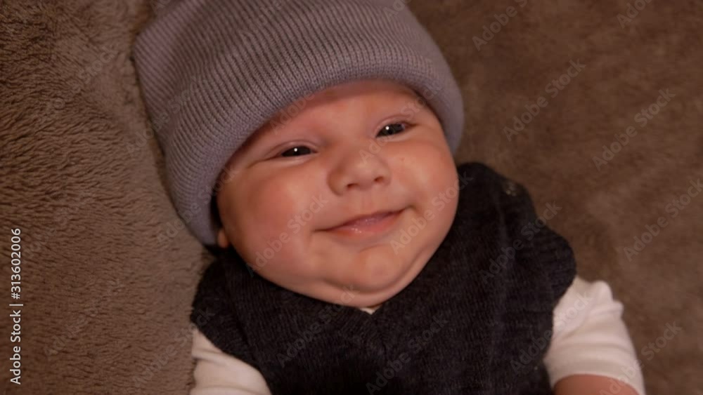 Little adorable black-eyed smiling baby in a gray hat is looking at the camera Little adorable black-eyed smiling baby in a gray hat is looking at the camera