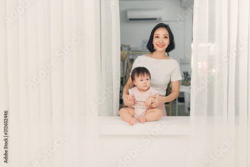 Mother and daughter sitting on sill near window