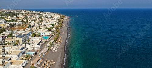 Aerial drone ultra wide top down photo of organised sandy beach in Kamari village, Santorini island, Cyclades, Greece