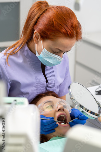 The dentist using the mirrors shows the girl the patient the condition of her teeth.