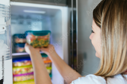 Woman placing container with frozen mixed vegetables in freezer.