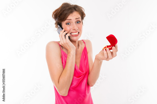 lovely surprised caucasian girl with a box with a ring in her hands calls on a telon and reports joy on a white background