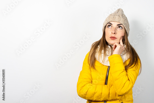 Young woman in a yellow down jacket and hat with a pensive face on a light background. Concept dream, thought, choice, decision, planning. Banner