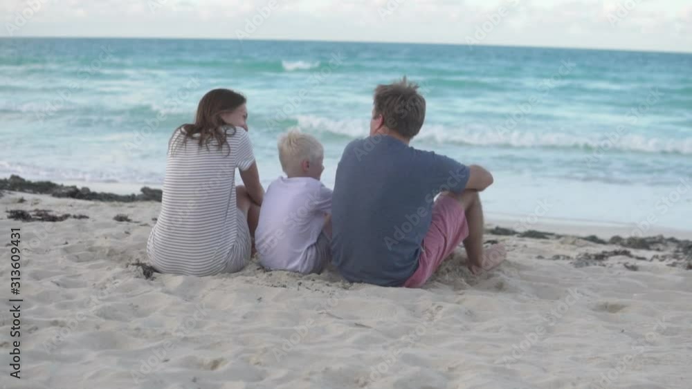 The family sits on the beach and looks at the ocean. View from the back The family sits on the beach and looks at the ocean. View from the back