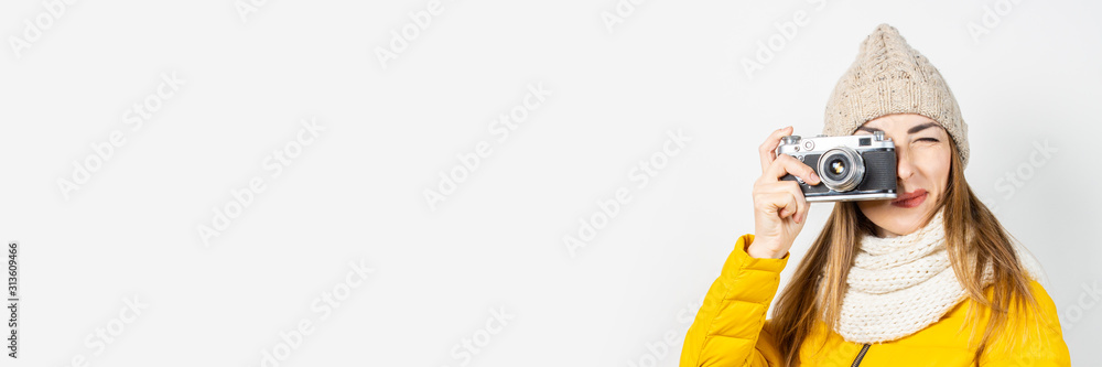 Young woman in a yellow down jacket and hat holds a camera in her hands and takes a picture on a light background. Concept of beauty and fashion, winter, autumn, technology. Banner Young woman in a yellow down jacket and hat holds a camera in her hands and takes a picture on a light background. Concept of beauty and fashion, winter, autumn, technology. Banner