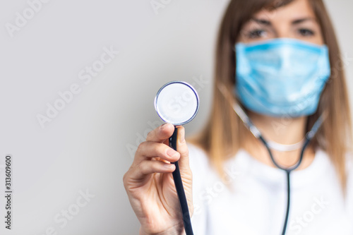 Young woman in a medical mask holds a stethoscope on a light background. Banner. Concept doctor, high level medical medicine, vaccination, visit to the doctor