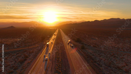DRONE: Scenic shot of 18 wheeler trucks and cars crossing Mojave desert at dusk