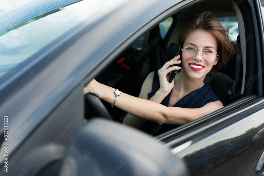 business woman with red lips in a classic suit sitting on the driver's seat in the car and talking on the phone