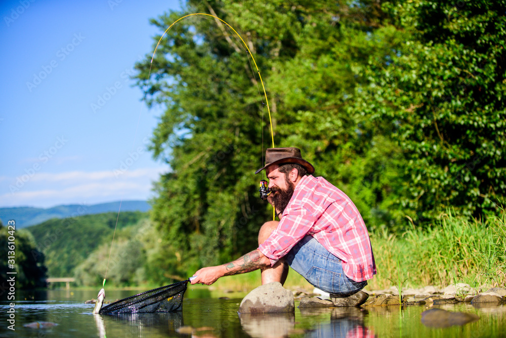 hipster fishing with spoon-bait. mature bearded man with fish on rod. successful fisherman in lake water. fly fish hobby. Summer activity. big game fishing. relax on nature. It is a big fish hipster fishing with spoon-bait. mature bearded man with fish on rod. successful fisherman in lake water. fly fish hobby. Summer activity. big game fishing. relax on nature. It is a big fish
