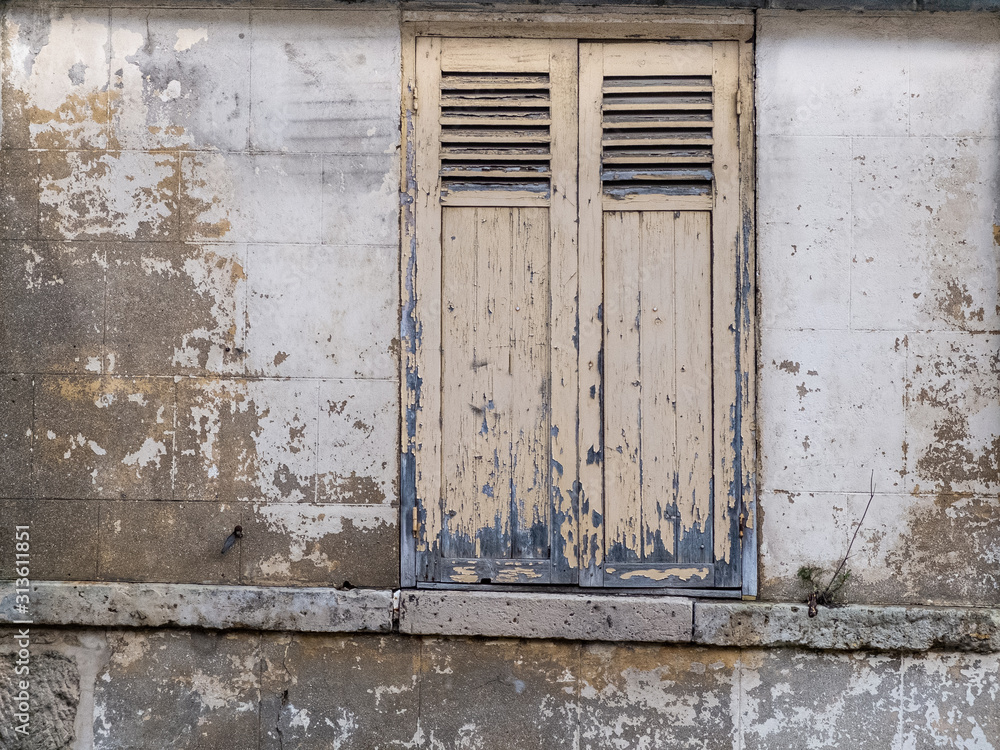 old concrete wall with crumbling white paint and old windows with the shutters closed