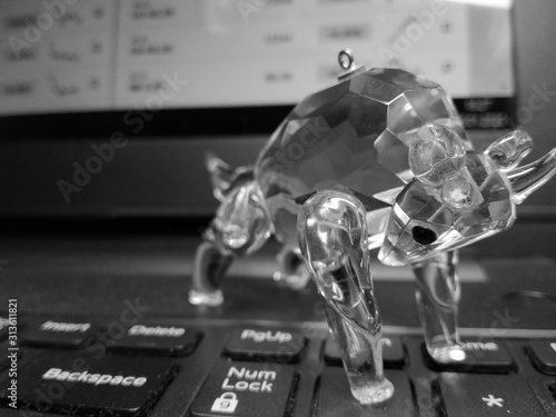 Crystal bull on the keyboard of the laptop against the background of the display with stock quotes and graphs