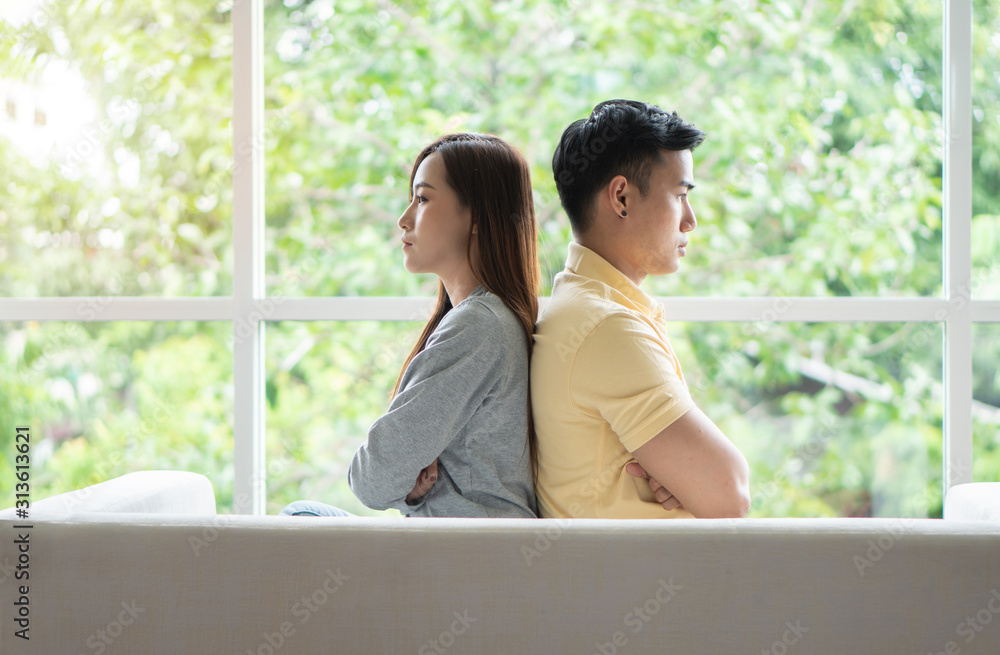 Unhappy Couple sitting behind each other on the couch and avoid talking or looking at each other, Cause of relationship problems and having misunderstanding or disagreement. Family problems concept Unhappy Couple sitting behind each other on the couch and avoid talking or looking at each other, Cause of relationship problems and having misunderstanding or disagreement. Family problems concept