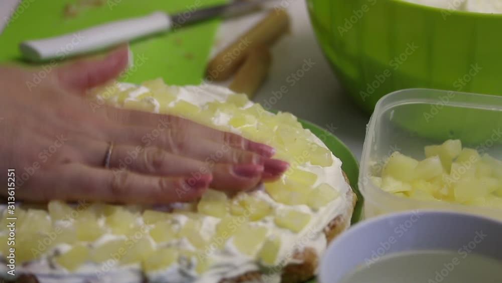 A woman makes a cake from Savoiardi cookies. Lays pineapple on cream. Near pineapples and cream. A woman makes a cake from Savoiardi cookies. Lays pineapple on cream. Near pineapples and cream.