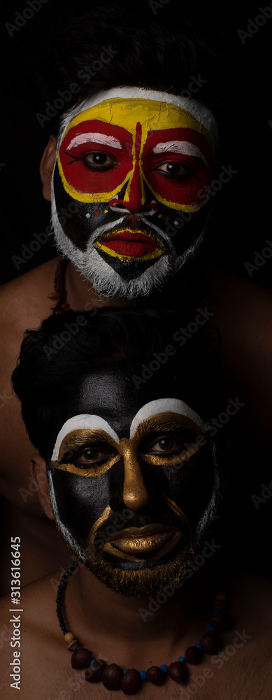Indian brunette men with their faces painted by vibrant colors like a tribe standing in front of a black studio copy space background. Indian hi fashion. Indian brunette men with their faces painted by vibrant colors like a tribe standing in front of a black studio copy space background. Indian hi fashion.