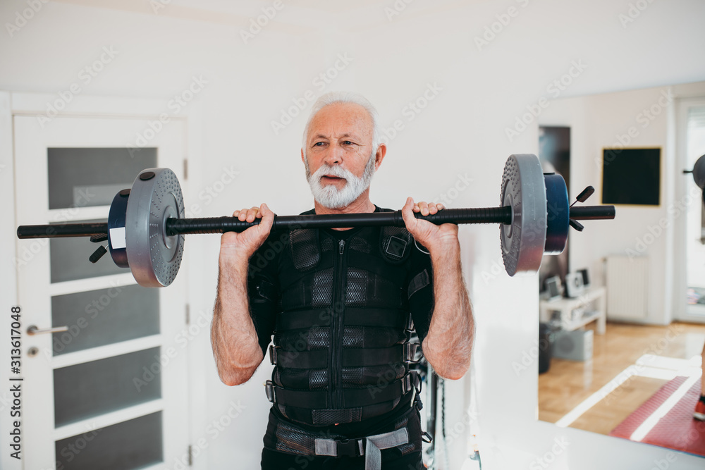 Nice looking and positive senior man doing exercises in electrical muscular stimulation suit. Nice looking and positive senior man doing exercises in electrical muscular stimulation suit.