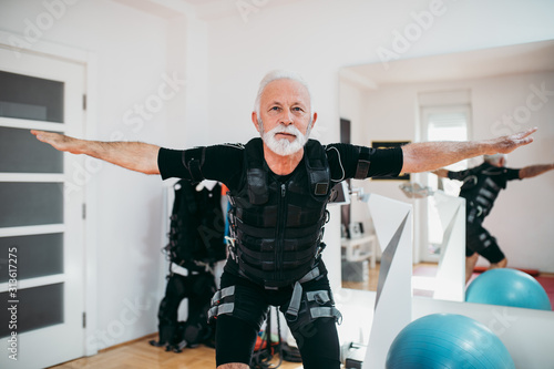 Nice looking and positive senior man doing exercises in electrical muscular stimulation suit. photo