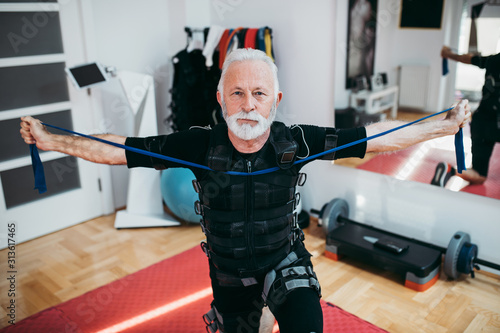 Nice looking and positive senior man doing exercises in electrical muscular stimulation suit.