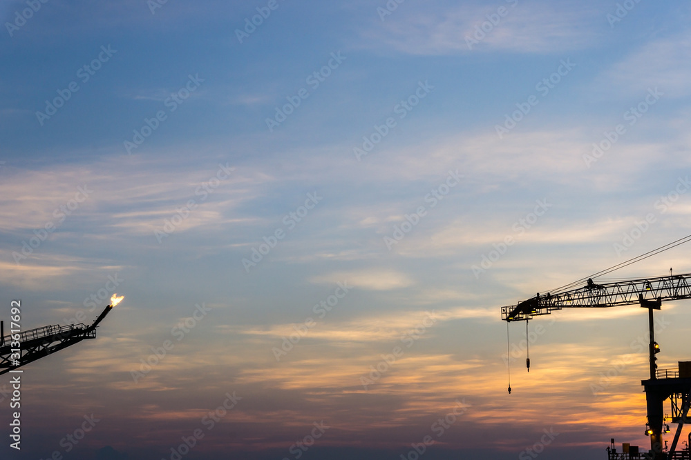 Obraz premium Tip of crane and flare of production platforms at oil field during sunset