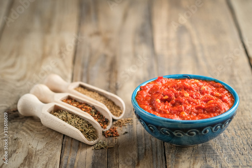 Traditional spicy harissa sauce in oriental bowl on rustic light background with spices. Maghreb cuisine.