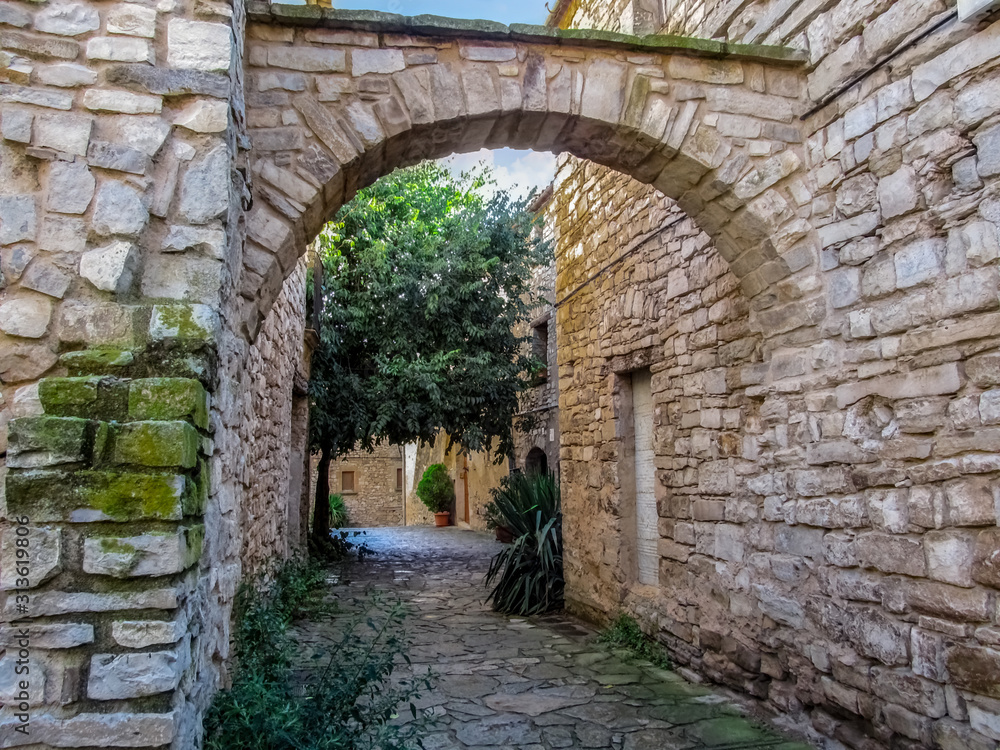 Spain, Montfalco Murallat - October 10, 2018: Street with green plants  and arched partition between stone walls in Montfalco Murallat village (Lleida, Catalonia). Inside a medieval spanish fortress