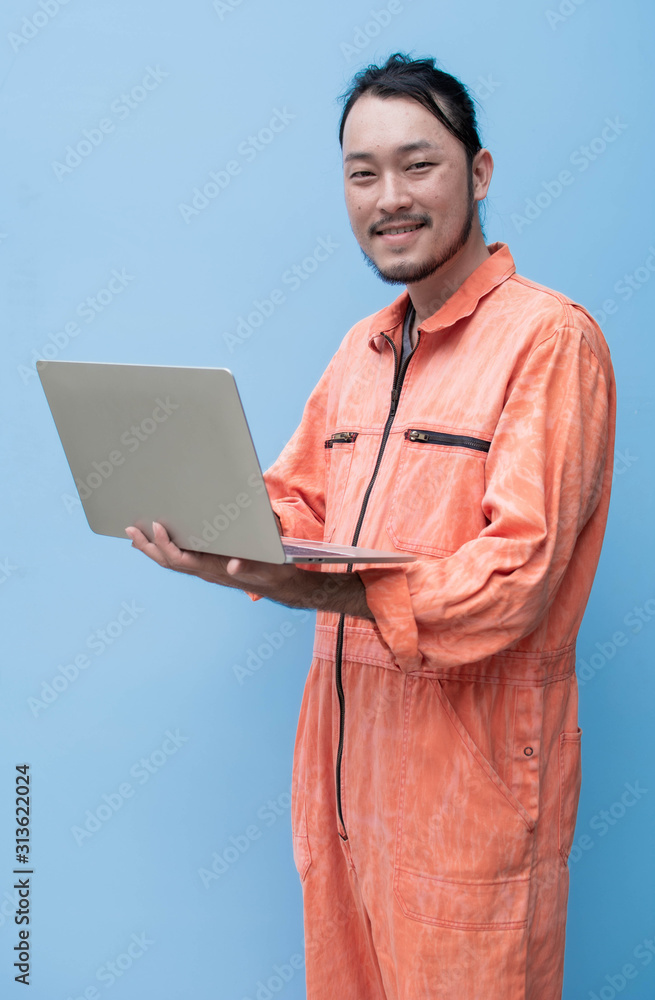 A man wearing mechanic suit is holding laptop A man wearing mechanic suit is holding laptop