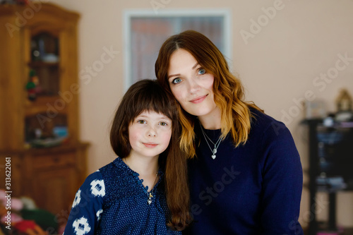 Adorable little school girl with beautiful young mother. Happy healthy family portrait, mom love and happiness, hugging and kissing. Woman and cute child.