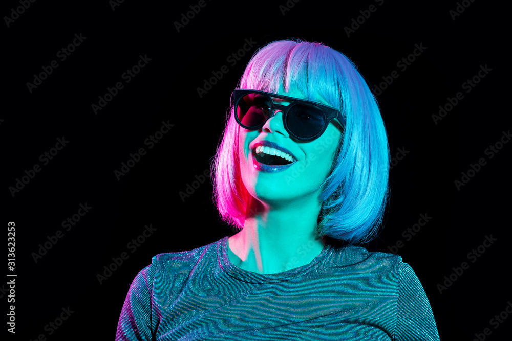 nightlife, fashion and people concept - happy young woman wearing pink wig and black sunglasses in neon ultra violet light over black background