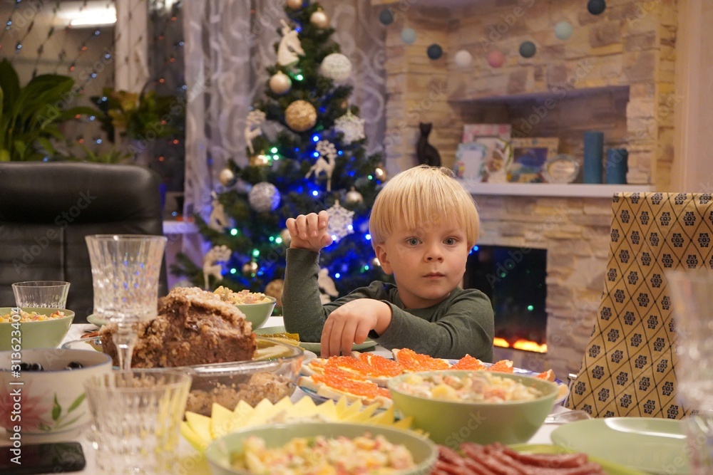 A child of three years in front of the festive table. New Year's holiday table. Salads, meat, alcohol on the New Year's table. A child of three years in front of the festive table. New Year's holiday table. Salads, meat, alcohol on the New Year's table.