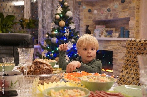 A child of three years in front of the festive table. New Year's holiday table. Salads, meat, alcohol on the New Year's table.
