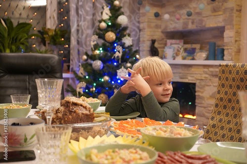 A child of three years in front of the festive table. New Year's holiday table. Salads, meat, alcohol on the New Year's table.