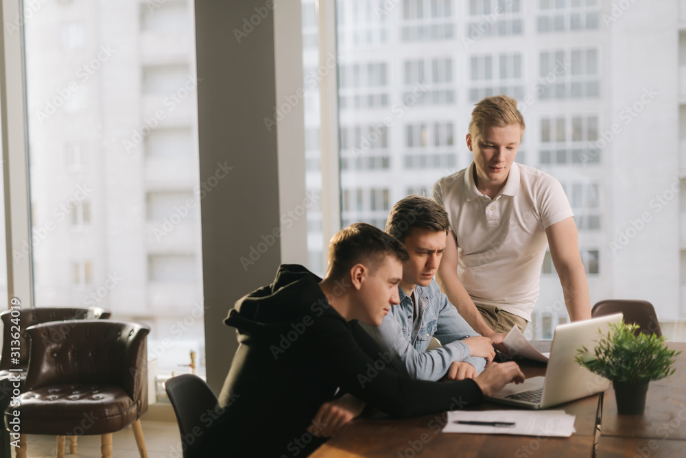 Group of young entrepreneurs having casual talk during meeting at the table with laptop in modern trendy office. Concept of teamwork young business people. Group of young entrepreneurs having casual talk during meeting at the table with laptop in modern trendy office. Concept of teamwork young business people.