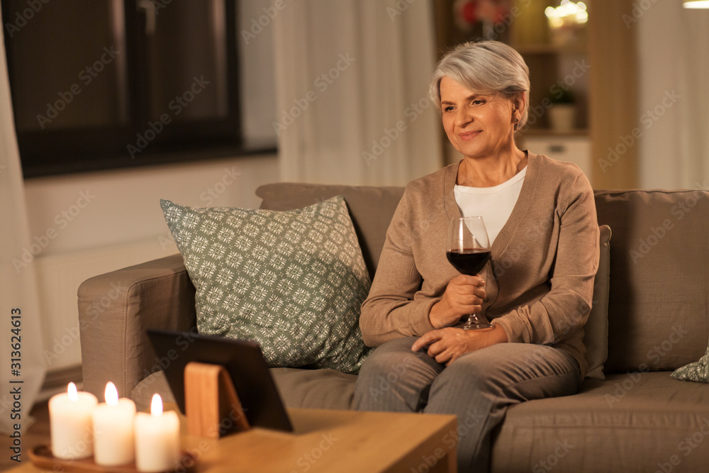 technology, old age and people concept - happy senior woman watching movie on tablet pc computer and drinking red wine at home in evening technology, old age and people concept - happy senior woman watching movie on tablet pc computer and drinking red wine at home in evening